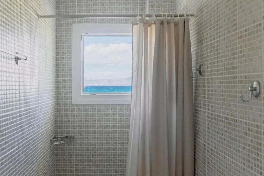 Modern shower at Kamini Apartments Kavos with neutral mosaic tiles and a window offering a stunning direct view of the Ionian Sea.