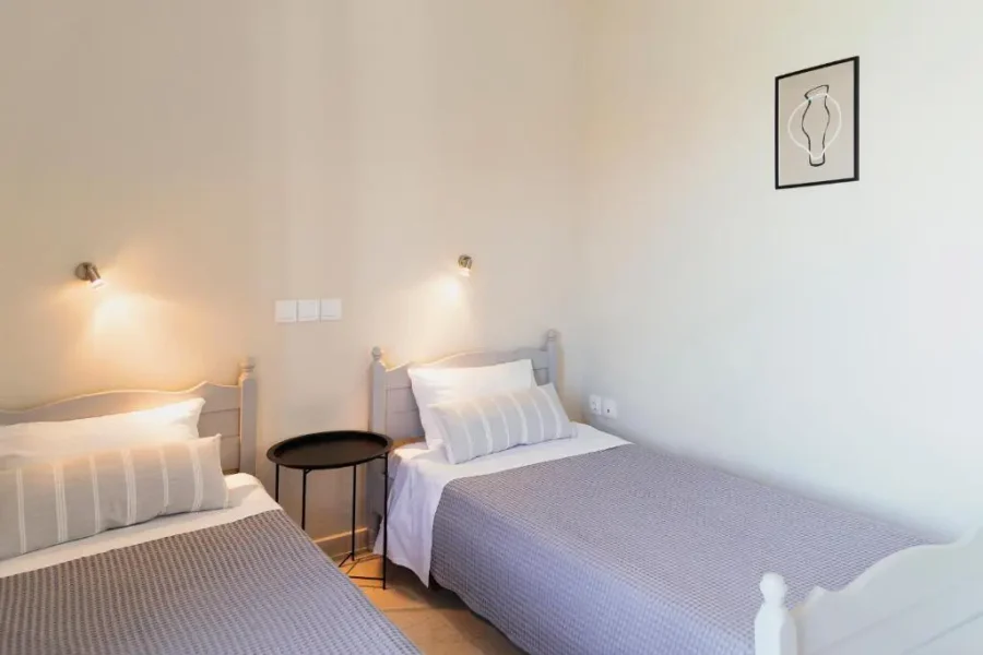 Twin bedroom setup at Kamini Apartments Kavos featuring two single beds with grey waffle-knit linens, individual reading lamps, and modern minimalist decor.