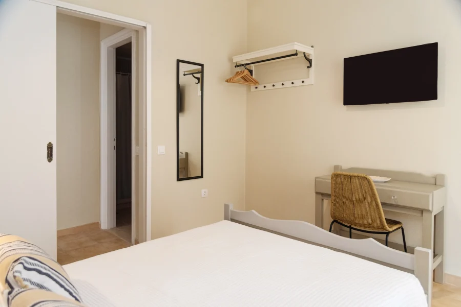 Bright bedroom at Kamini Apartments Corfu featuring minimalist storage, a wicker desk chair, and neutral Mediterranean decor.