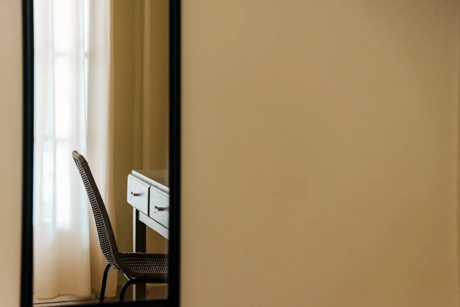 Artistic mirror reflection of a minimalist wicker chair and wooden desk at Kamini Apartments Kavos, showcasing the boutique Mediterranean interior design.