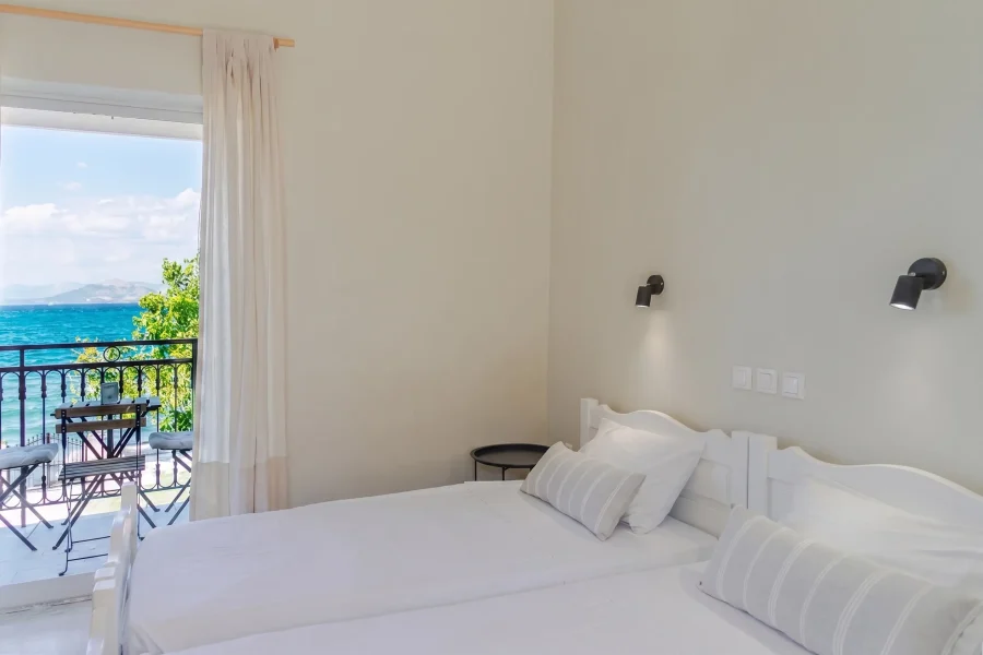 Panoramic Ionian sea view from a private balcony with white curtains, featuring a small wooden table and chairs at Kamini Apartments in Kavos, Corfu.