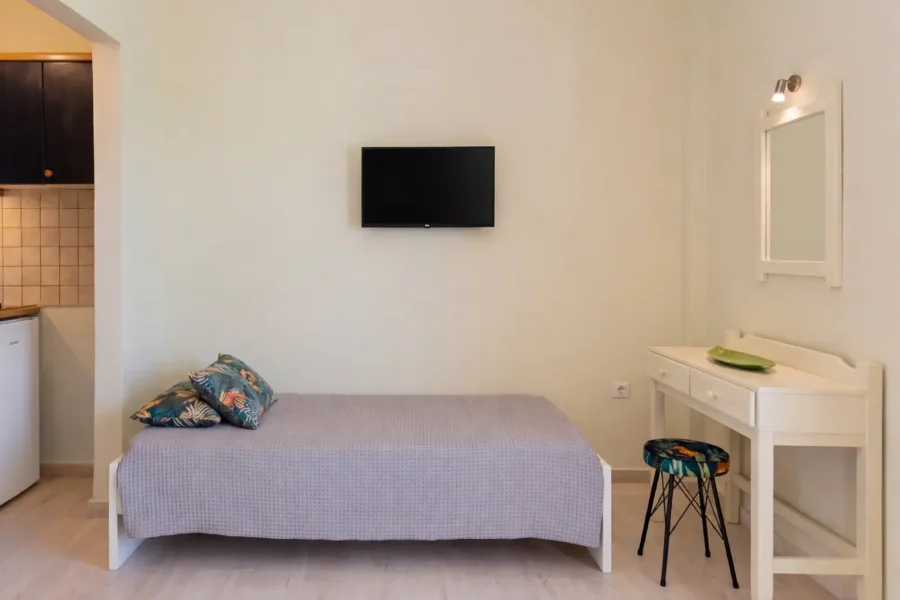 Bright and clean studio interior at Kamini Apartments in Kavos, Corfu, featuring twin beds with white linens, an outdoor wooden dining set, and marble flooring.