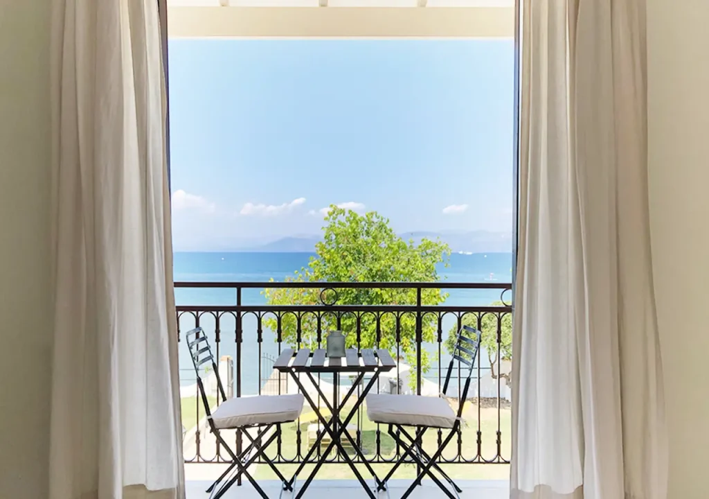 Private balcony at Kamini Apartments Kavos with outdoor bistro seating and a panoramic view of the Ionian Sea and mainland Greece.