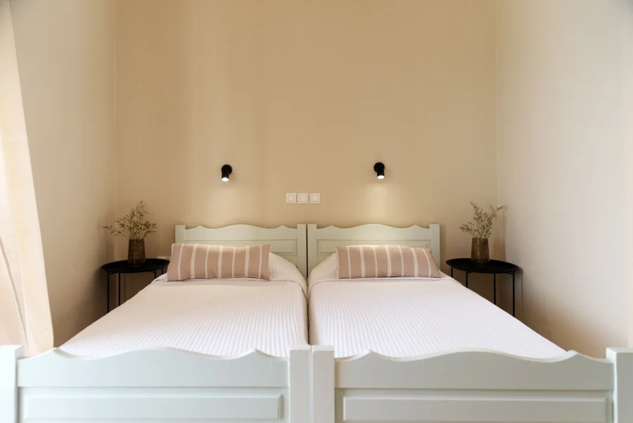 Symmetrical view of twin beds at Kamini Apartments Kavos with minimalist decor, individual reading lamps, and bedside tables in a bright studio.