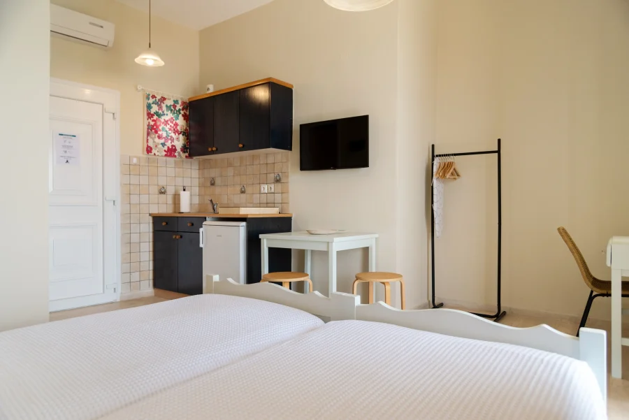 Open-plan studio at Kamini Apartments Kavos featuring a kitchenette with fridge, dining table, air conditioning, and twin beds.