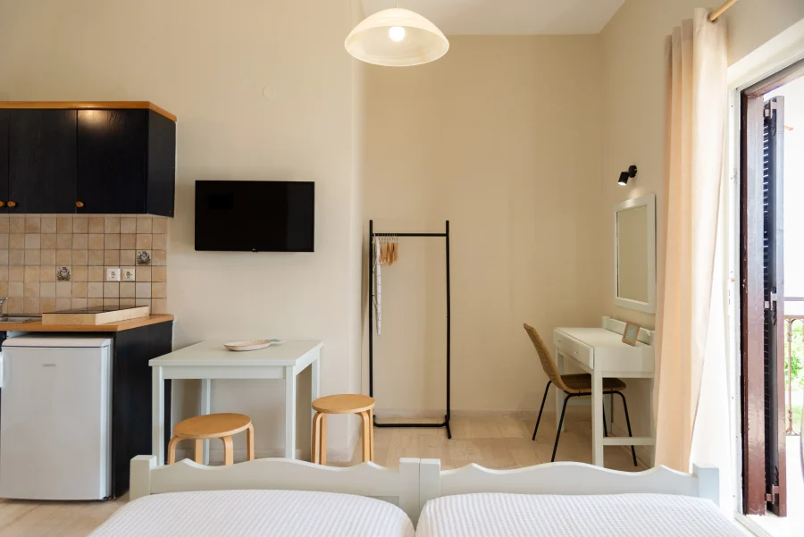 Bright studio apartment at Kamini Apartments Kavos featuring a dedicated desk area, flat-screen TV, and a compact kitchenette with a dining table.