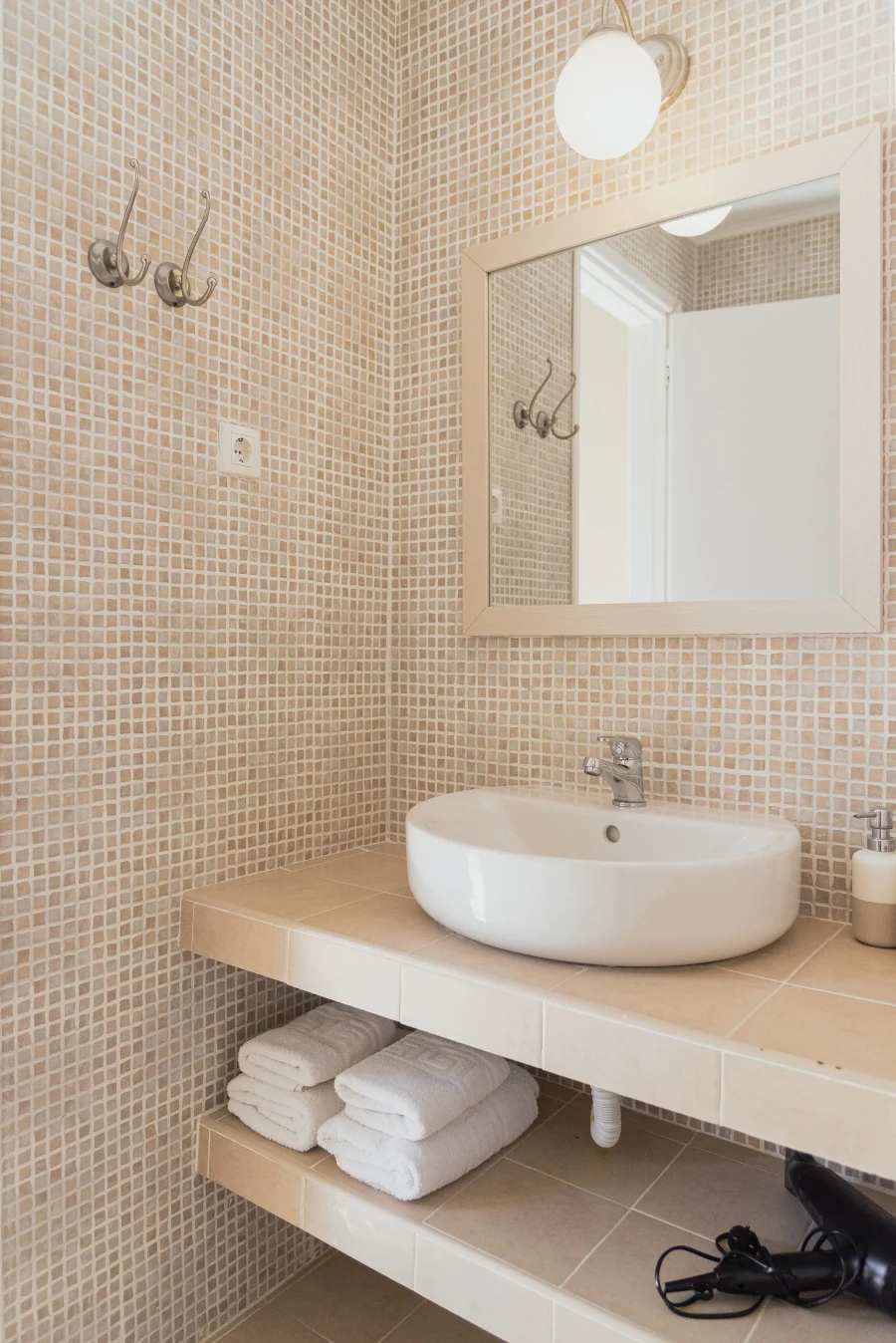 Modern ensuite bathroom at Kamini Apartments Kavos featuring a washbasin, large mirror, fresh white towels, and a provided hairdryer.