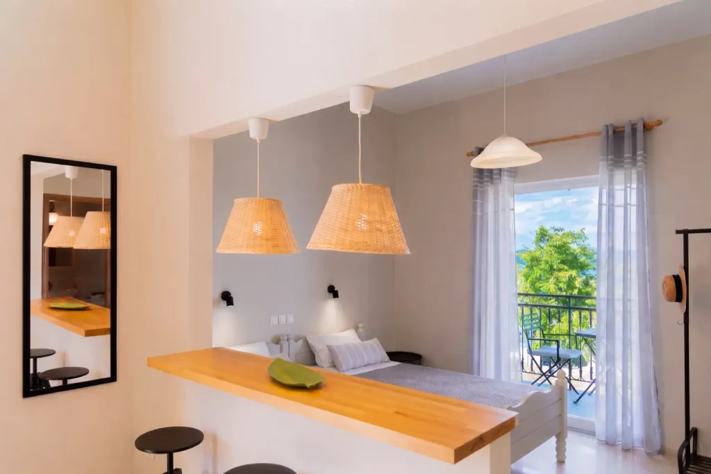 Kamini Apartments Corfu self-catering studio interior showing the open-plan dining area, twin beds, and bright terrace access.