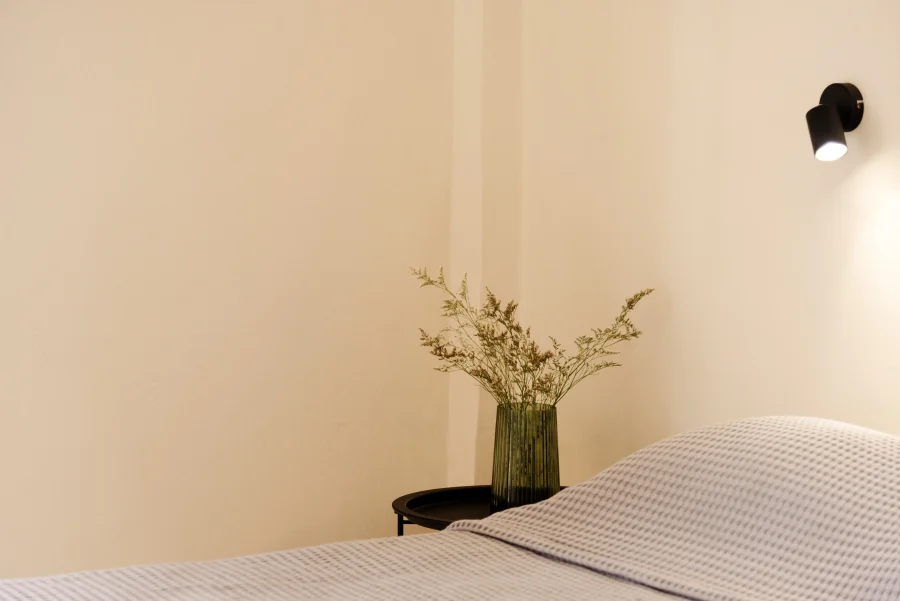 Minimalist bedroom detail at Kamini Apartments Kavos featuring a sleek black reading lamp, bedside table with a decorative vase, and clean waffle-knit bedding.