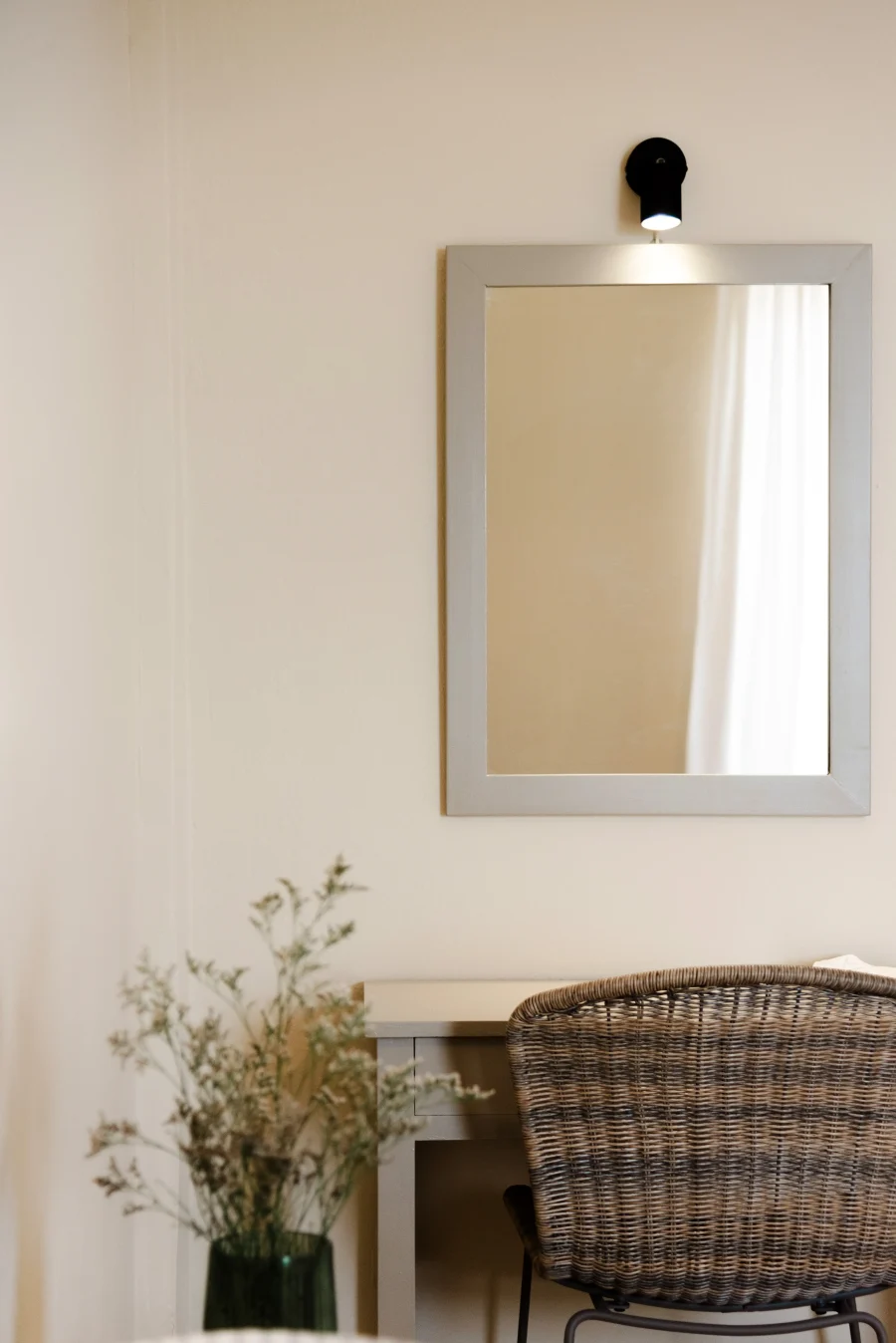 Modern vanity area at Kamini Apartments Kavos featuring a woven wicker chair, large wall mirror with dedicated lighting, and minimalist desk.