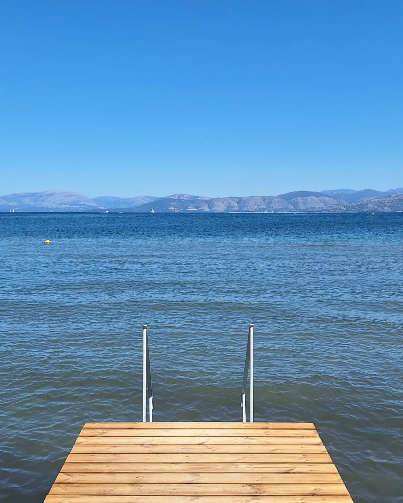 A private pier at Kamini Apartments in Kavos, Corfu, leading into the calm, shallow waters of the Ionian Sea.