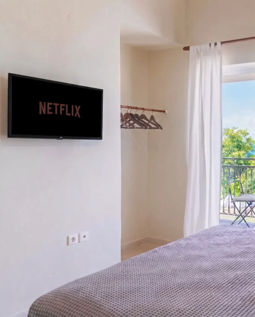 Modern wall-mounted Smart TV with Netflix in a bright studio at Kamini Apartments, Kavos, featuring minimalist decor and a view toward the private balcony.